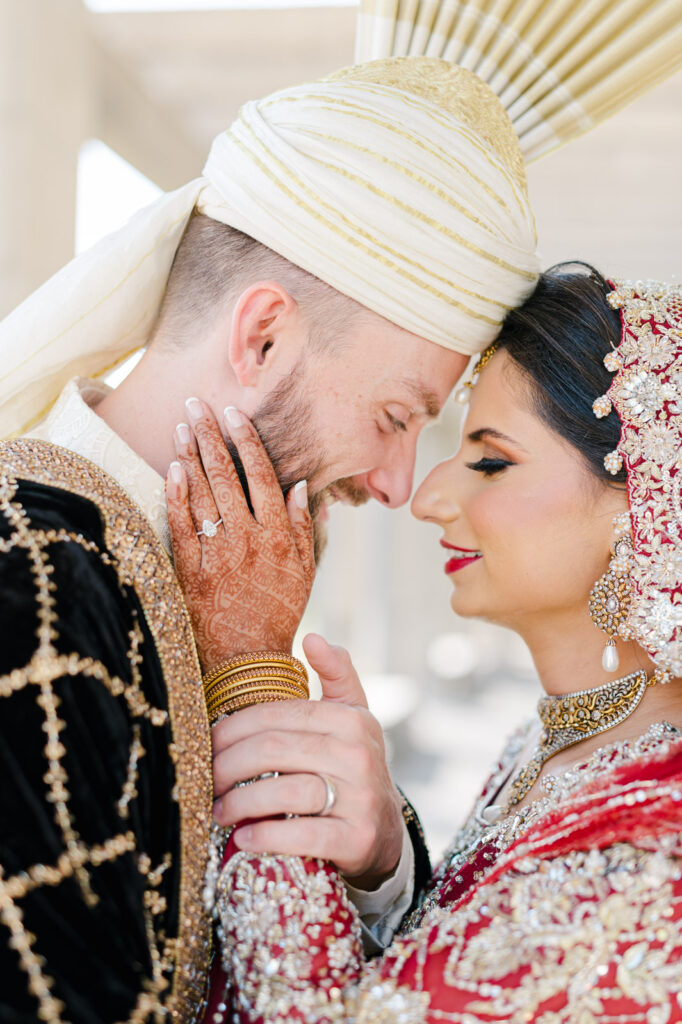 close up image of a couple in their traditional pakistani attire, touching foreheads and hands